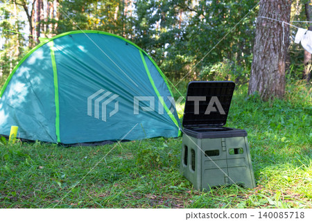 Portable camping toilet in front of tent, field area usage, outdoor comfort and convenience, tourism and travel facility in nature. 140085718