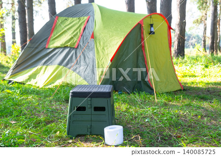 Portable camping toilet by yellow-green tent, outdoor comfort, sanitation for travel and tourism, application in wild nature area. 140085725