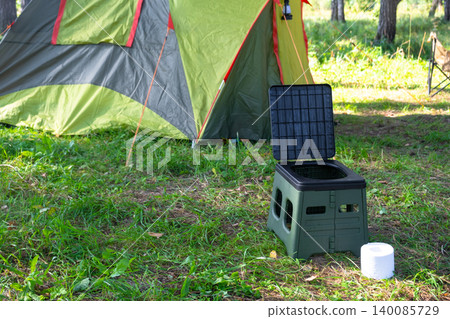 Portable toilet and tissue near tent, travel comfort and hygiene in wild campsite, camping convenience, area of use nature tourism. 140085729