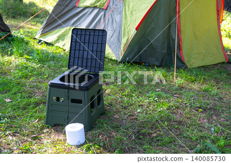 Modern portable toilet and roll on forest campsite, area use for camping and travel hygiene, convenience in wild outdoor tourism. Modern portable toilet and roll on forest campsite, area use for camping and travel hygiene, convenience in wild outdoor tourism. 140085730