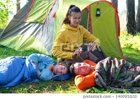 Mother uses bug spray on children, camping tent, outdoor travel, family safety, insect bite prevention, healthy lifestyle event. Mother uses bug spray on children, camping tent, outdoor travel, family safety, insect bite prevention, healthy lifestyle event. 140085820