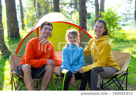 Family enjoying picnic at yellow tent: mom, dad and daughter in sporty clothes, vacation in the forest. Family enjoying picnic at yellow tent: mom, dad and daughter in sporty clothes, vacation in the forest. 140085853