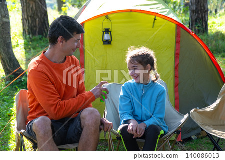 Father explaining mosquito bite risks to daughter, family at outdoor campsite, raising awareness of bite allergy, skin safety, healthy habits in summer setting. Father explaining mosquito bite risks to daughter, family at outdoor campsite, raising awareness of bite allergy, skin safety, healthy habits in summer setting. 140086013