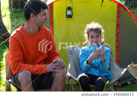 Father and daughter at campsite, child applying mosquito repellent, focus on skin protection, allergy avoidance, outdoor safety, family wellness, summer scene. Father and daughter at campsite, child applying mosquito repellent, focus on skin protection, allergy avoidance, outdoor safety, family wellness, summer scene. 140086015