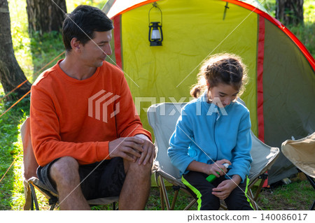 Father handing mosquito repellent to daughter, child protected outdoors, family by tent, allergy and illness prevention, caring emotions, summer adventure. Father handing mosquito repellent to daughter, child protected outdoors, family by tent, allergy and illness prevention, caring emotions, summer adventure. 140086017