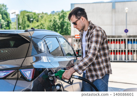 Young man refueling modern crossover vehicle at self service gas station 140086601
