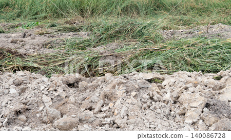 Textured shot of freshly tilled. Cloddy dirt ground covered partially with cut green grass and weeds showcasing agricultural soil preparation or rural landscape development. Textured shot of freshly tilled. Cloddy dirt ground covered partially with cut green grass and weeds showcasing agricultural soil preparation or rural landscape development. 140086728