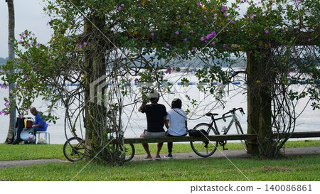 Couple Relaxing by Lake Under Blooming Purple Vine Arbor Couple Relaxing by Lake Under Blooming Purple Vine Arbor 140086861