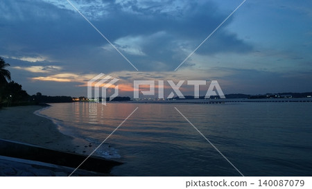 Tropical Twilight Coastline with Reflective Sea and Distant City 140087079