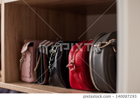 Collection of stylish women's fashion handbags sitting neatly on a wooden shelf, organizing accessories in an elegant closet Collection of stylish women's fashion handbags sitting neatly on a wooden shelf, organizing accessories in an elegant closet 140087293