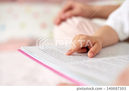Child's hand with pointing finger reading a storybook, engaging with written text, symbolizing early education and literacy 140087303