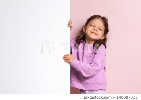 Young girl peeking from behind a large white sign, providing space for advertising, text, or promotional content Young girl peeking from behind a large white sign, providing space for advertising, text, or promotional content 140087313