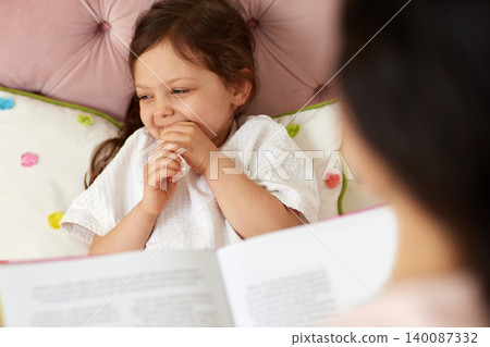 Little girl smiling, covering her mouth with hands, while listening to a story being read from a book during bedtime Little girl smiling, covering her mouth with hands, while listening to a story being read from a book during bedtime 140087332
