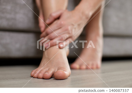 Person experiencing discomfort, touching an aching ankle. Reflecting pain, inflammation, and need for healthcare and recovery 140087337