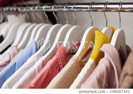 Row of colorful clothes hanging on white wooden hangers in an organized closet. Concepts of fashion, retail, and shopping Row of colorful clothes hanging on white wooden hangers in an organized closet. Concepts of fashion, retail, and shopping 140087341