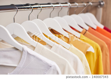Row of various color shirts, from white to orange, displayed on white hangers on a chrome clothing rack Row of various color shirts, from white to orange, displayed on white hangers on a chrome clothing rack 140087343