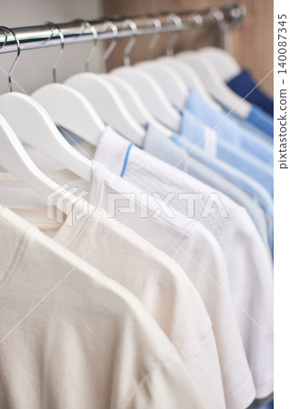 Clothes on white wooden hangers hanging on metal rail. Shirts arranged in a color gradient from off-white to blue Clothes on white wooden hangers hanging on metal rail. Shirts arranged in a color gradient from off-white to blue 140087345