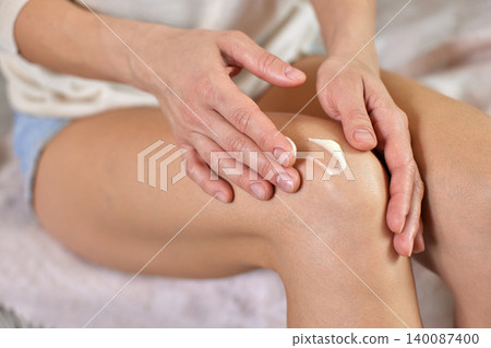 Woman's hands applying white moisturizing cream to her knee, providing skincare, muscle relaxation, and joint pain relief Woman's hands applying white moisturizing cream to her knee, providing skincare, muscle relaxation, and joint pain relief 140087400