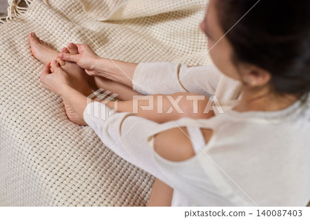 Woman massaging her own foot, practicing self-care and reflexology for relaxation and wellness at home Woman massaging her own foot, practicing self-care and reflexology for relaxation and wellness at home 140087403