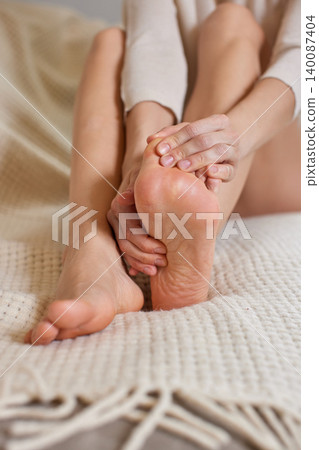 Woman self-massaging her sore foot, experiencing discomfort and seeking relief and comfort after a long day Woman self-massaging her sore foot, experiencing discomfort and seeking relief and comfort after a long day 140087404