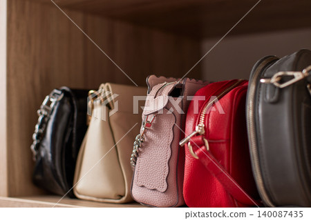 Collection of stylish women's fashion handbags sitting neatly on a wooden shelf, organizing accessories in an elegant closet Collection of stylish women's fashion handbags sitting neatly on a wooden shelf, organizing accessories in an elegant closet 140087435