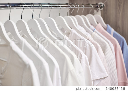 Clothes hanging on white wooden hangers in a neat wardrobe. Displaying minimalist fashion and organized storage Clothes hanging on white wooden hangers in a neat wardrobe. Displaying minimalist fashion and organized storage 140087436