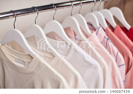 Row of various shirts hanging on white hangers on a metal rail inside a closet, showing organization and neatness Row of various shirts hanging on white hangers on a metal rail inside a closet, showing organization and neatness 140087439
