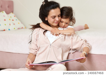 Mother reading a storybook to daughter, sharing a moment of bonding, love, and education in a cozy home setting Mother reading a storybook to daughter, sharing a moment of bonding, love, and education in a cozy home setting 140087468