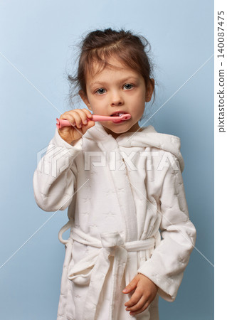 child girl brushing teeth wearing white bathrobe promoting hygiene, daily dental care and routine child girl brushing teeth wearing white bathrobe promoting hygiene, daily dental care and routine 140087475