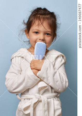 happy little child girl in a white bathrobe holding a blue hairbrush happy little child girl in a white bathrobe holding a blue hairbrush 140087477