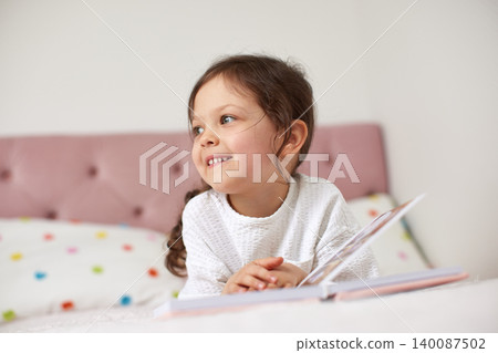 little child girl smiling and enjoying a storybook while relaxing in bed, embracing childhood learning and happiness at home little child girl smiling and enjoying a storybook while relaxing in bed, embracing childhood learning and happiness at home 140087502