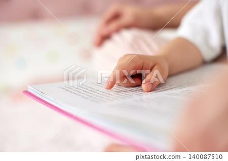 Baby's hand indicating text in a pink book, learning to read with a parent, focusing on early education and literacy Baby's hand indicating text in a pink book, learning to read with a parent, focusing on early education and literacy 140087510