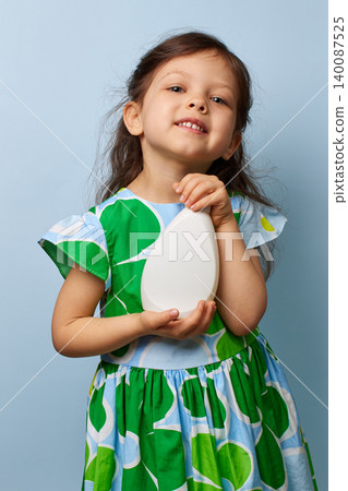 Little child girl smiling, proudly presenting a blank white bottle against a blue background 140087525