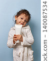 cute child girl in white bathrobe holding blank cosmetic tube, representing childhood hygiene and skincare 140087534