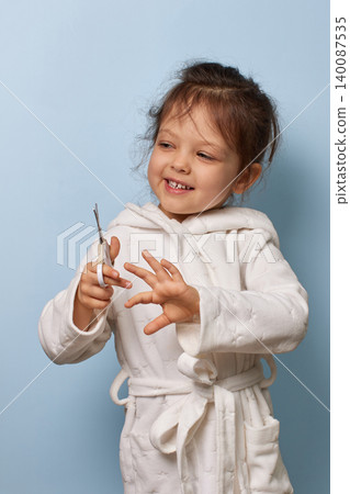 happy child girl in a white bathrobe learning self-care with nail scissors happy child girl in a white bathrobe learning self-care with nail scissors 140087535