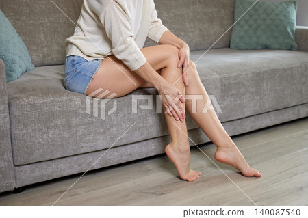 Woman on sofa applying moisturizer to legs, self-massage for soft, hydrated skin and relaxed at-home beauty and wellness routine Woman on sofa applying moisturizer to legs, self-massage for soft, hydrated skin and relaxed at-home beauty and wellness routine 140087540
