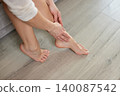 Woman experiencing leg pain and discomfort, massaging her aching ankle and tired feet at home, seeking relief 140087542