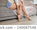 Woman sitting on sofa, touching her leg and ankle feeling discomfort and pain. Concepts of healthcare, injury relief, and muscle ache 140087548