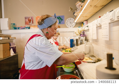 Caucasian senior woman preparing food in a commercial restaurant kitchen Caucasian senior woman preparing food in a commercial restaurant kitchen 140088113