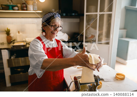 Active Hispanic Senior Woman Making Homemade Pasta in Professional Kitchen Studio Active Hispanic Senior Woman Making Homemade Pasta in Professional Kitchen Studio 140088114