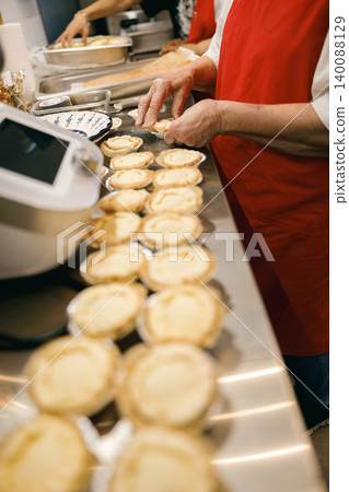Mature Caucasian senior woman preparing handmade tarts in a bright professional bakery kitchen. Mature Caucasian senior woman preparing handmade tarts in a bright professional bakery kitchen. 140088129
