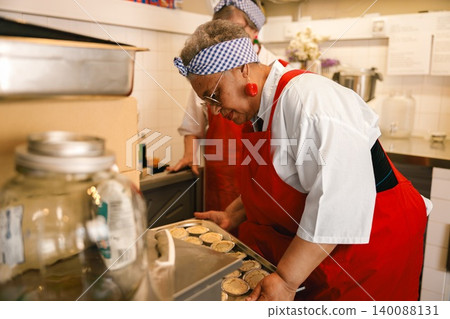 Senior Black woman carefully preparing freshly baked pies in a professional commercial kitchen Senior Black woman carefully preparing freshly baked pies in a professional commercial kitchen 140088131