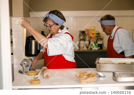 Active senior Caucasian and Black women handcrafting fresh pasta dough in a bright kitchen Active senior Caucasian and Black women handcrafting fresh pasta dough in a bright kitchen 140088138