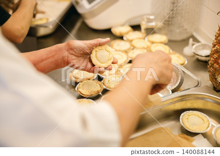 Caucasian senior baker preparing small dough pastries in a commercial kitchen 140088144