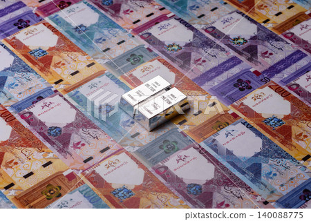 A silver bar, white metal against a backdrop of Qatari money, as a concept. A silver bar A silver bar, white metal against a backdrop of Qatari money, as a concept. A silver bar 140088775