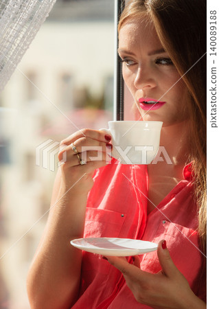 Woman looking through window, relaxing drinking coffee Woman looking through window, relaxing drinking coffee 140089188