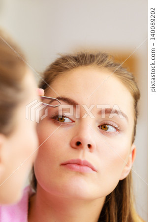 Woman tweezing eyebrows plucking with tweezers Woman tweezing eyebrows plucking with tweezers 140089202