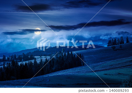 mountain landscape in september at night. full moon over green nature of carpathian mountains with coniferous forest. view of a scenery with rolling hills under cloudy sky. pasture near woods mountain landscape in september at night. full moon over green nature of carpathian mountains with coniferous forest. view of a scenery with rolling hills under cloudy sky. pasture near woods 140089293