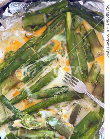 Baked asparagus with eggs and melted cheese sits on foil with fork in close food preparation scene. Top view of asparagus meal, cooking, diet, nutrition, kitchen dinner, home recipe Baked asparagus with eggs and melted cheese sits on foil with fork in close food preparation scene. Top view of asparagus meal, cooking, diet, nutrition, kitchen dinner, home recipe 140089756