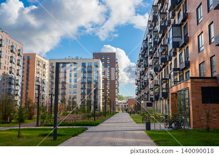 Modern residential building complex with apartment blocks and pedestrian walkway. Urban neighborhood design with landscaped courtyard, green grass and sky. Housing development for city living. Modern residential building complex with apartment blocks and pedestrian walkway. Urban neighborhood design with landscaped courtyard, green grass and sky. Housing development for city living. 140090018